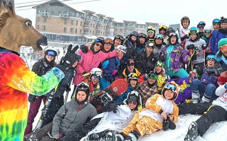 Members of Columbia's Ski and Snowboard Club, all wearing colorful gear, pose in the snow. 